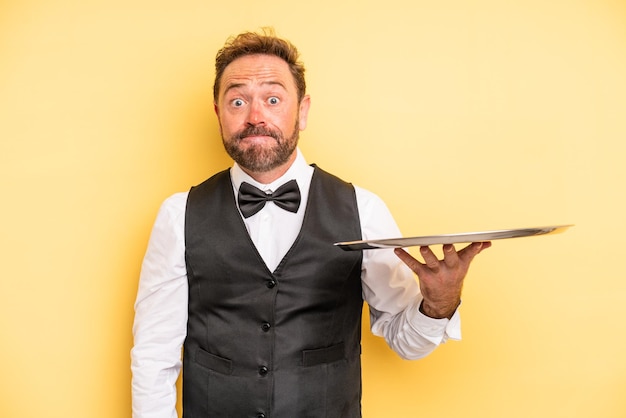 Middle age man shrugging, feeling confused and uncertain. waiter concept with tray