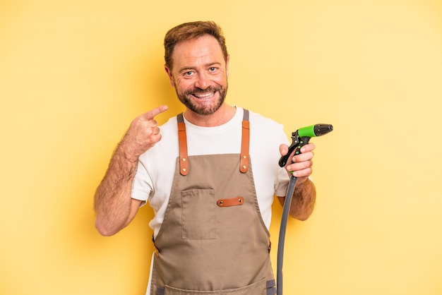 Middle age man smiling confidently pointing to own broad smile. gardener hose concept