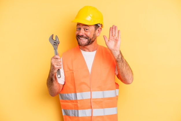 Middle age man smiling happily, waving hand, welcoming and greeting you.  breakdown car repair wrench concept