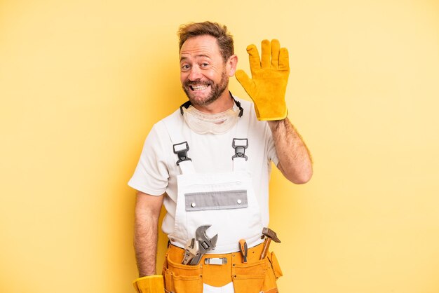 Middle age man smiling happily, waving hand, welcoming and greeting you. handyman and repair concept