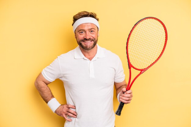 middle age man smiling happily with a hand on hip and confident. tennis concept