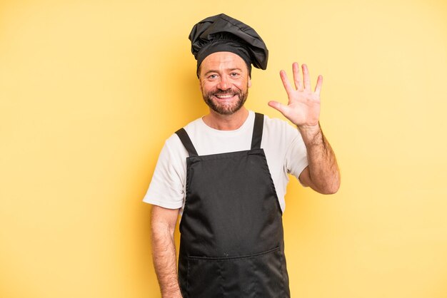 Middle age man smiling and looking friendly showing number five chef concept