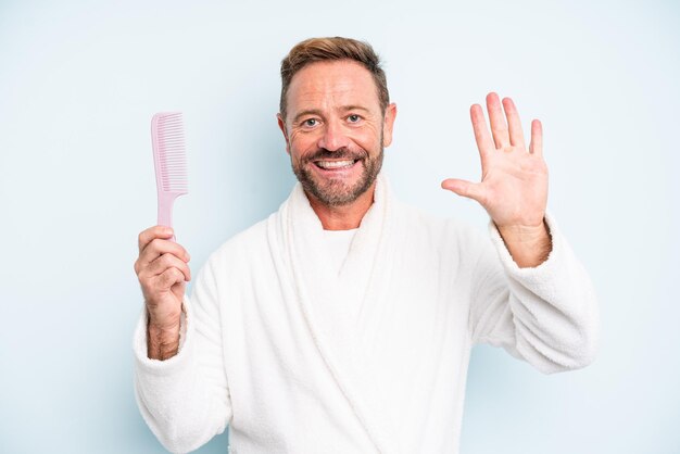 Middle age man smiling and looking friendly, showing number five. hair comb concept