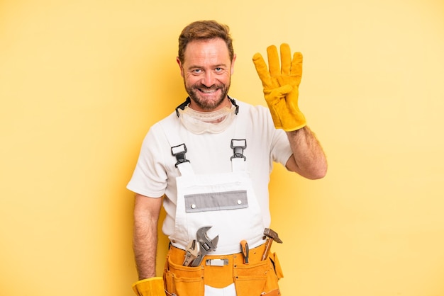 middle age man smiling and looking friendly, showing number four. handyman and repair concept