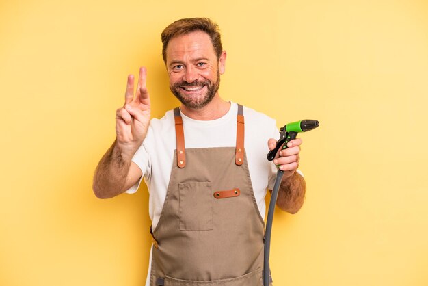 middle age man smiling and looking friendly, showing number three. gardener hose concept