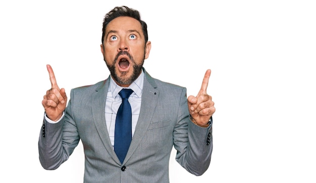 Middle age man wearing business clothes amazed and surprised looking up and pointing with fingers and raised arms.