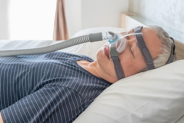 Middle age man wearing CPAP mask and headgear to help with his sleep apnea while sleeping in his bed