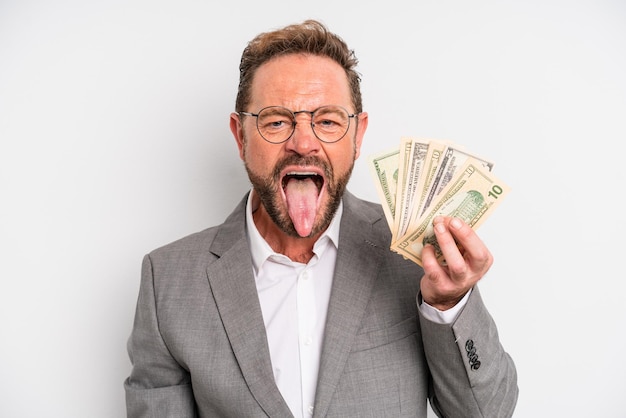 Middle age man with cheerful and rebellious attitude joking and sticking tongue out dollar banknotes concept