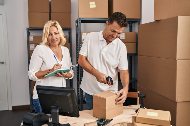 Middle age man and woman business partners scanning label using barcode reader working at storehouse