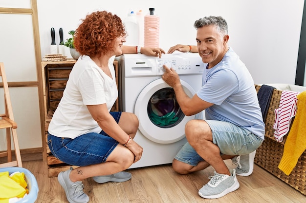 自信を持って笑みを浮かべて中年男性と女性カップル ランドリーで洗濯物をオンにします。