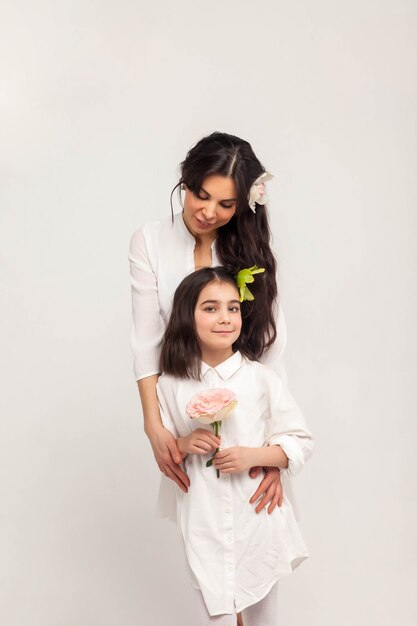 Middle age mother and young daughter in white clothes hold flower in hands