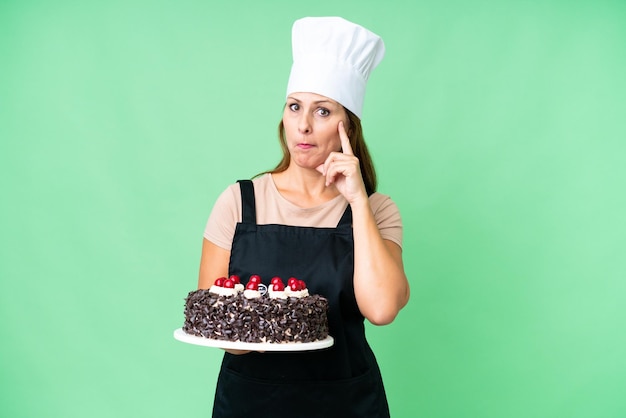 Шеф-повар средних лет держит большой торт на изолированном фоне, думая об идее