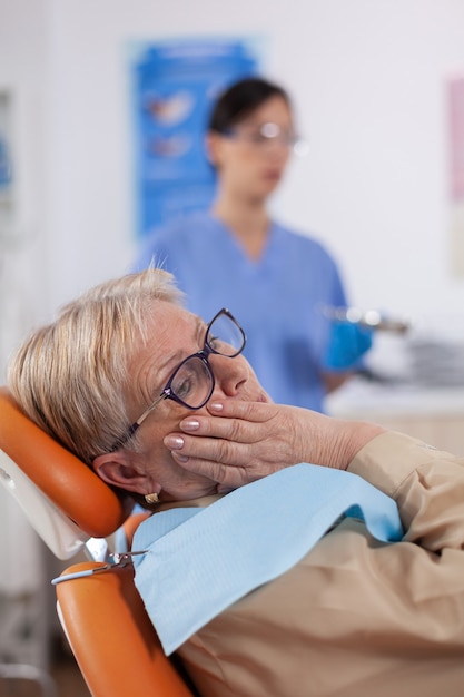 歯科医院の椅子に座って痛みを伴う表情で口に触れる中年患者