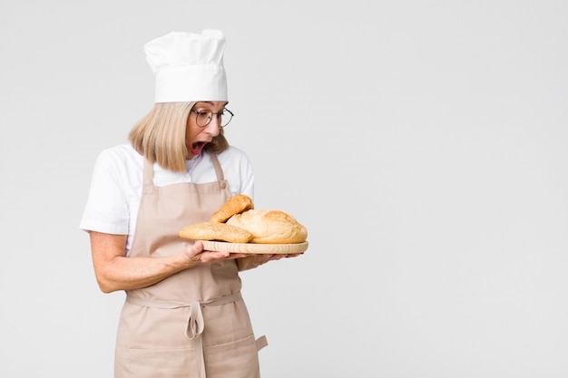 Женщина пекаря среднего возраста милая с хлебом против стены космоса экземпляра