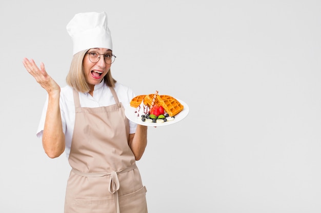 Middle age pretty baker  woman with waffles against copy space wall