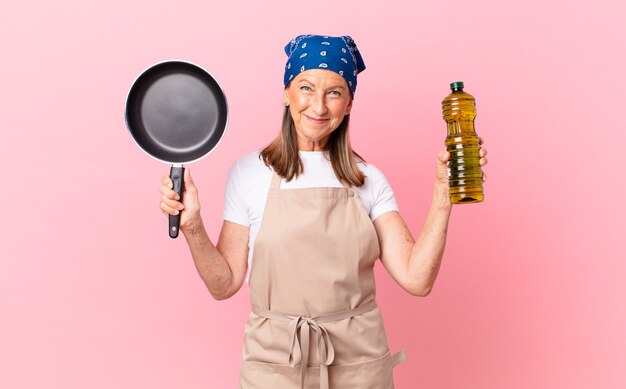 middle age pretty chef woman holding a pan and a olive oil bottle