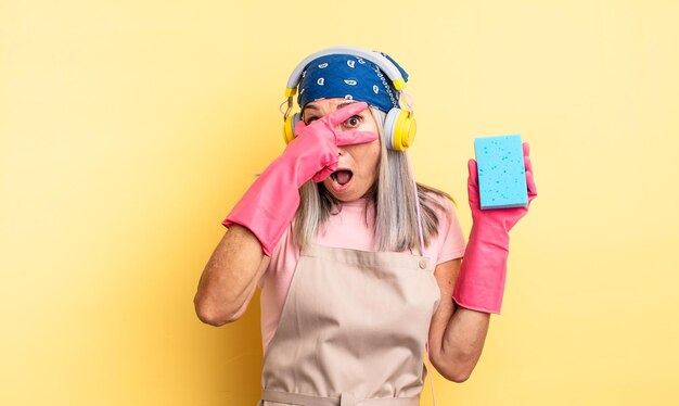 Middle age pretty woman looking shocked, scared or terrified, covering face with hand. scourer cleaner