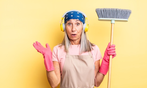 Foto bella donna di mezza età che sembra sorpresa e scioccata, con la mascella caduta in possesso di un oggetto. concetto di famiglia e scopa