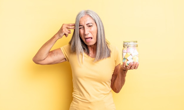 middle age pretty woman looking unhappy and stressed, suicide gesture making gun sign. candies bottle concept