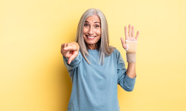 middle age pretty woman pointing at camera choosing you. hand bandage concept