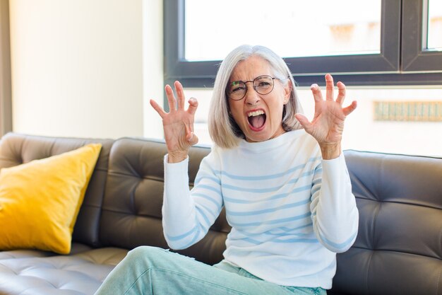 Middle age pretty woman screaming in panic or anger, shocked, terrified or furious, with hands next to head