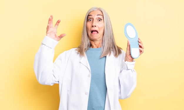 Middle age pretty woman screaming with hands up in the air. chiropodist concept