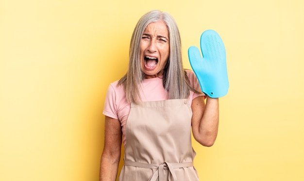 Middle age pretty woman shouting aggressively, looking very angry. oven mitt concept