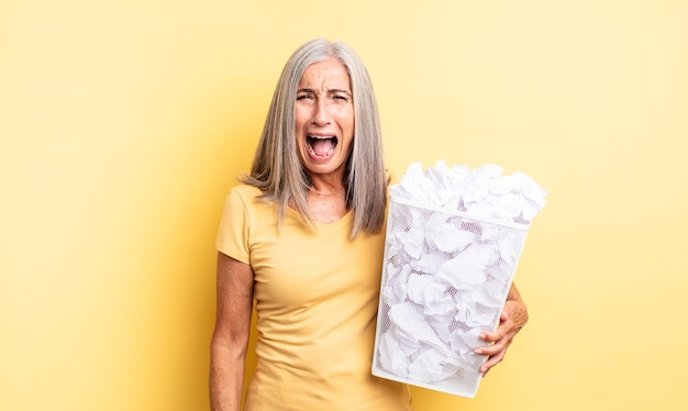 Middle age pretty woman shouting aggressively, looking very angry. paper balls failure concept