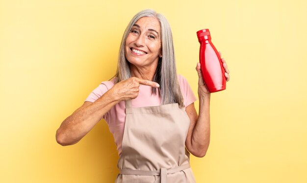 Middle age pretty woman smiling cheerfully, feeling happy and pointing to the side. ketchup concept