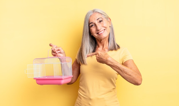 Middle age pretty woman smiling cheerfully, feeling happy and pointing to the side. pet cage or jail concept