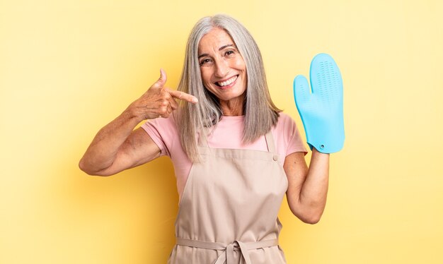 自信を持って笑顔を浮かべる中年のきれいな女性が自分の広い笑顔を指しています。オーブンミットのコンセプト