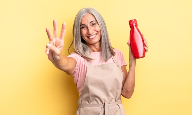 Donna graziosa di mezza età che sorride e che sembra amichevole che mostra il concetto di ketchup numero tre