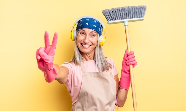 Middle age pretty woman smiling and looking friendly, showing number two. household and broom concept