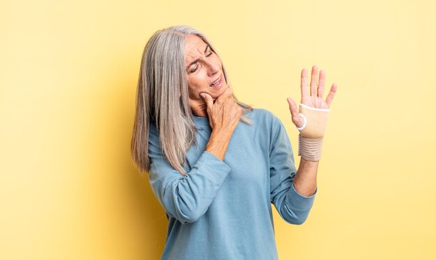 Middle age pretty woman smiling with a happy, confident expression with hand on chin. hand bandage concept