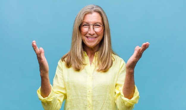 Middle age pretty woman with yellow shirt and eyeglasses on blue