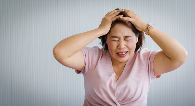 중년 아시아 여성은 갑작스러운 두통과 뇌졸증으로 고통을 느끼고 일그러진 얼굴로 머리를 잡고 있습니다. 두뇌와 머리 문제의 개념입니다.