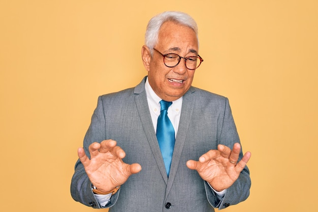 Middle age senior greyhaired handsome business man wearing glasses over yellow background disgusted expression displeased and fearful doing disgust face because aversion reaction