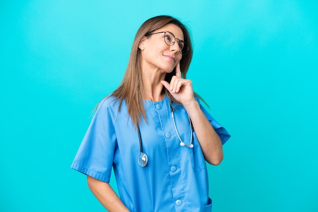 Middle age surgeon woman isolated on blue background thinking an idea while looking up