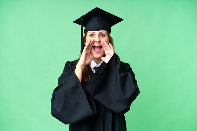 Middle age university graduate woman over isolated background shouting and announcing something