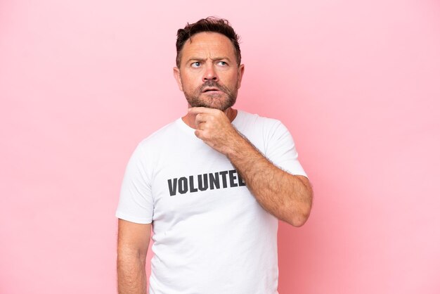 Middle age volunteer man isolated on pink background isolated on pink background having doubts