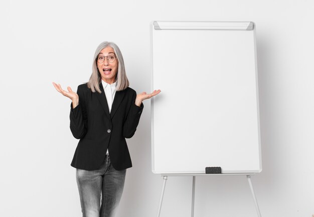 Middle age white hair woman feeling happy and astonished at something unbelievable and a board copy space. business concept