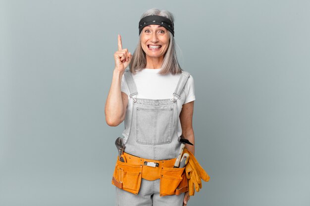 Middle age white hair woman feeling like a happy and excited genius after realizing an idea and wearing work wear and tools. housekeeping concept