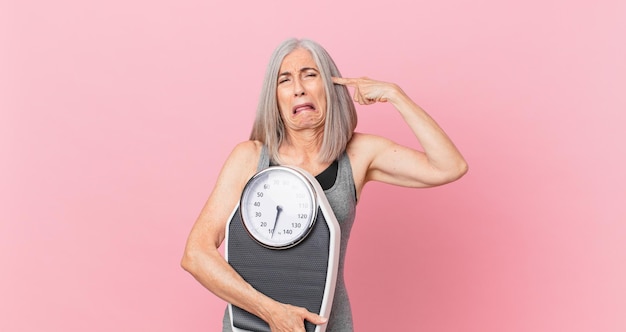 Middle age white hair woman holding a weight scale. fitness and diet concept