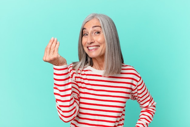 Middle age white hair woman making capice or money gesture, telling you to pay