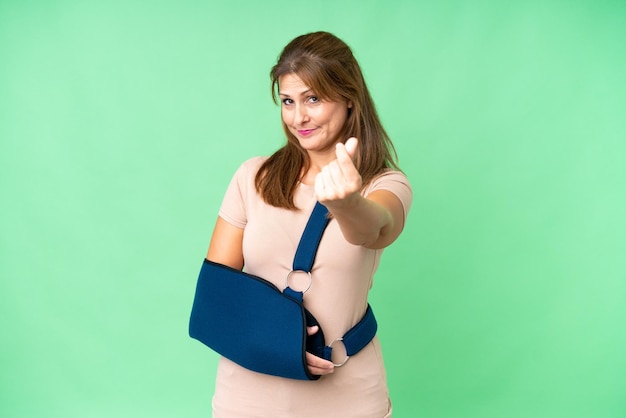 Middle age with broken arm and wearing a sling over isolated background making money gesture