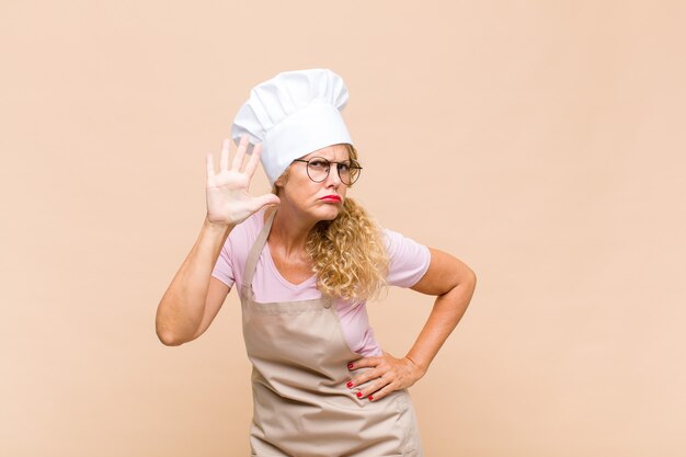 Photo middle age woman baker smiling and looking friendly, showing number five or fifth with hand forward, counting down