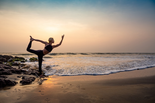 Middle age woman in black doing yoga on sand beach in India Natarajasana pose