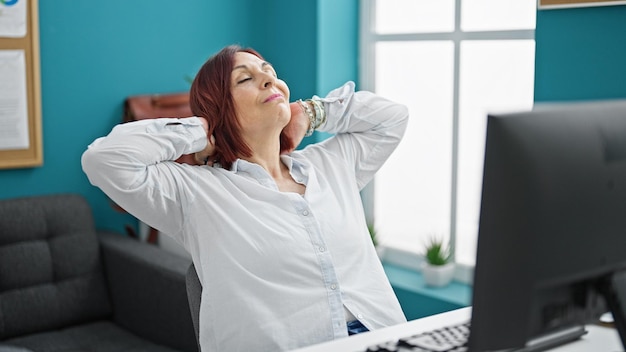 Middle age woman business worker relaxed with hands on head at the office