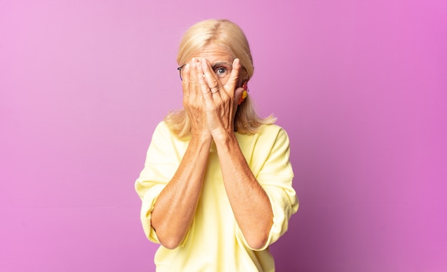 Middle age woman covering face with hands, peeking between fingers