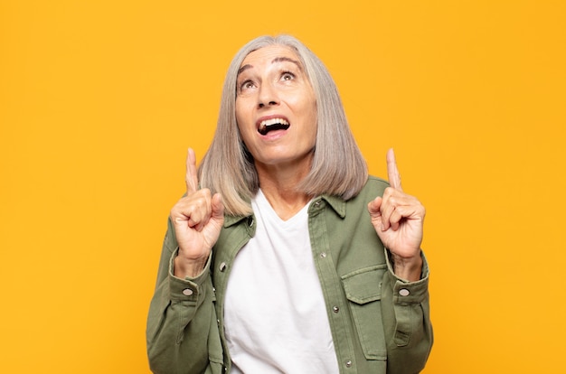 Middle age woman feeling awed and open mouthed pointing upwards with a shocked and surprised look